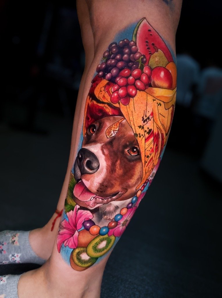 Tatuaje a color de retrato de perro con sombrero de frutas carnavalesco en la pierna