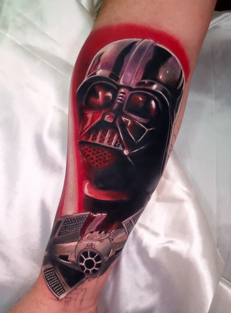 Tatuaje a color de Darth Vader y nave TIE Fighter en el antebrazo con fondo rojo