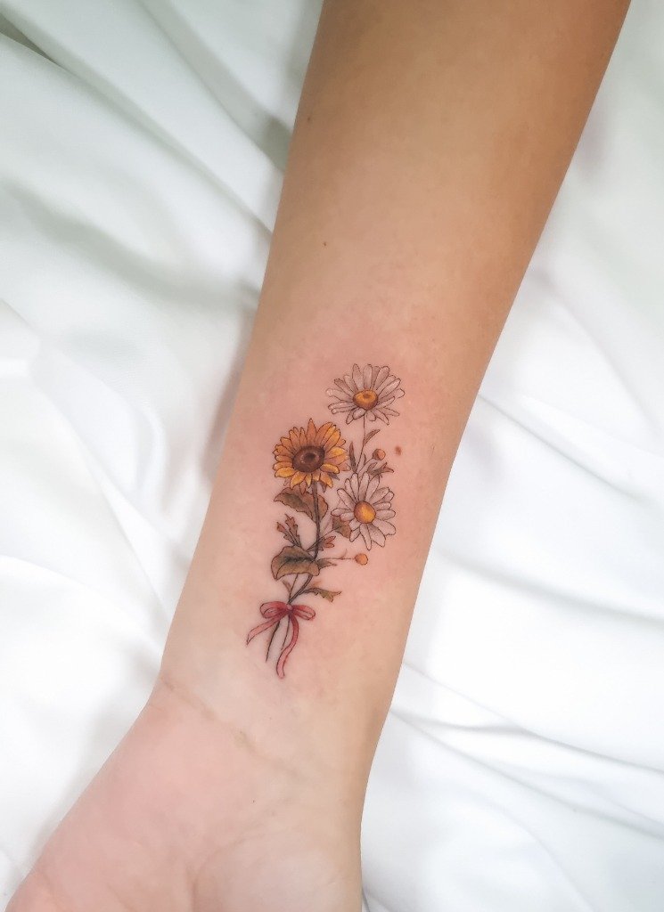 Tatuaje fine line a color de ramillete de girasol y margaritas con cinta en la muñeca